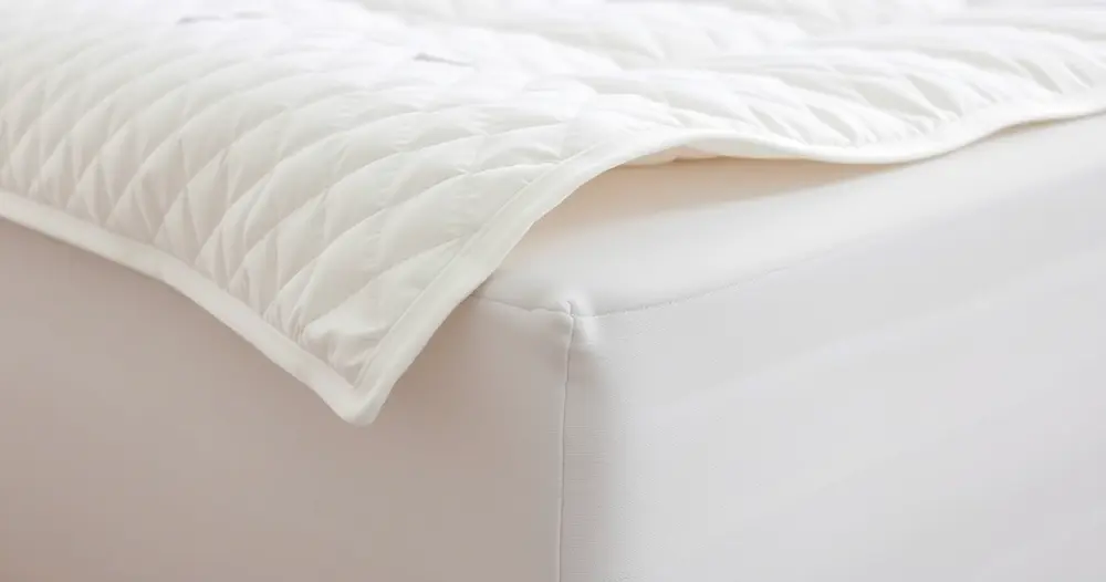 Mãos ajustando uma capa protetora branca sobre o colchão de uma cama