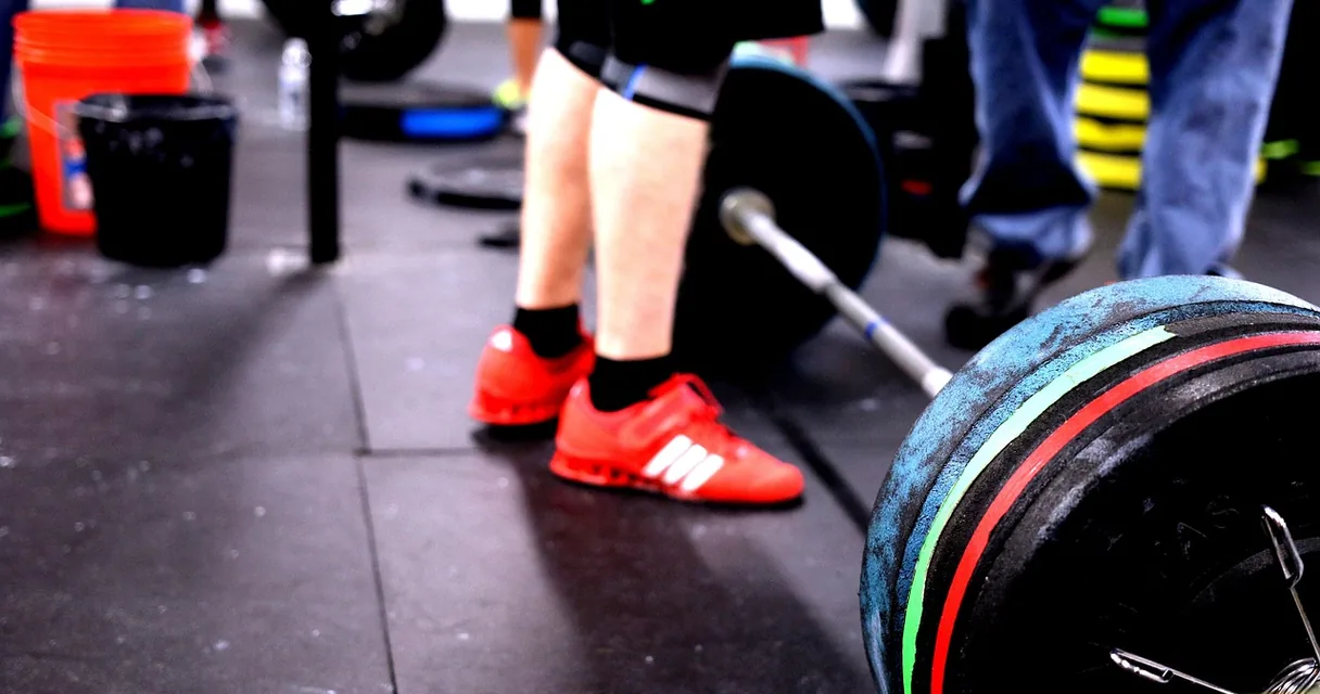 Atleta de crossfit ao lado de barra com anilhas no box